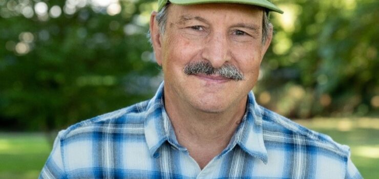 portrait of Jim Myers, wearing a green hat and blue plaid shirt